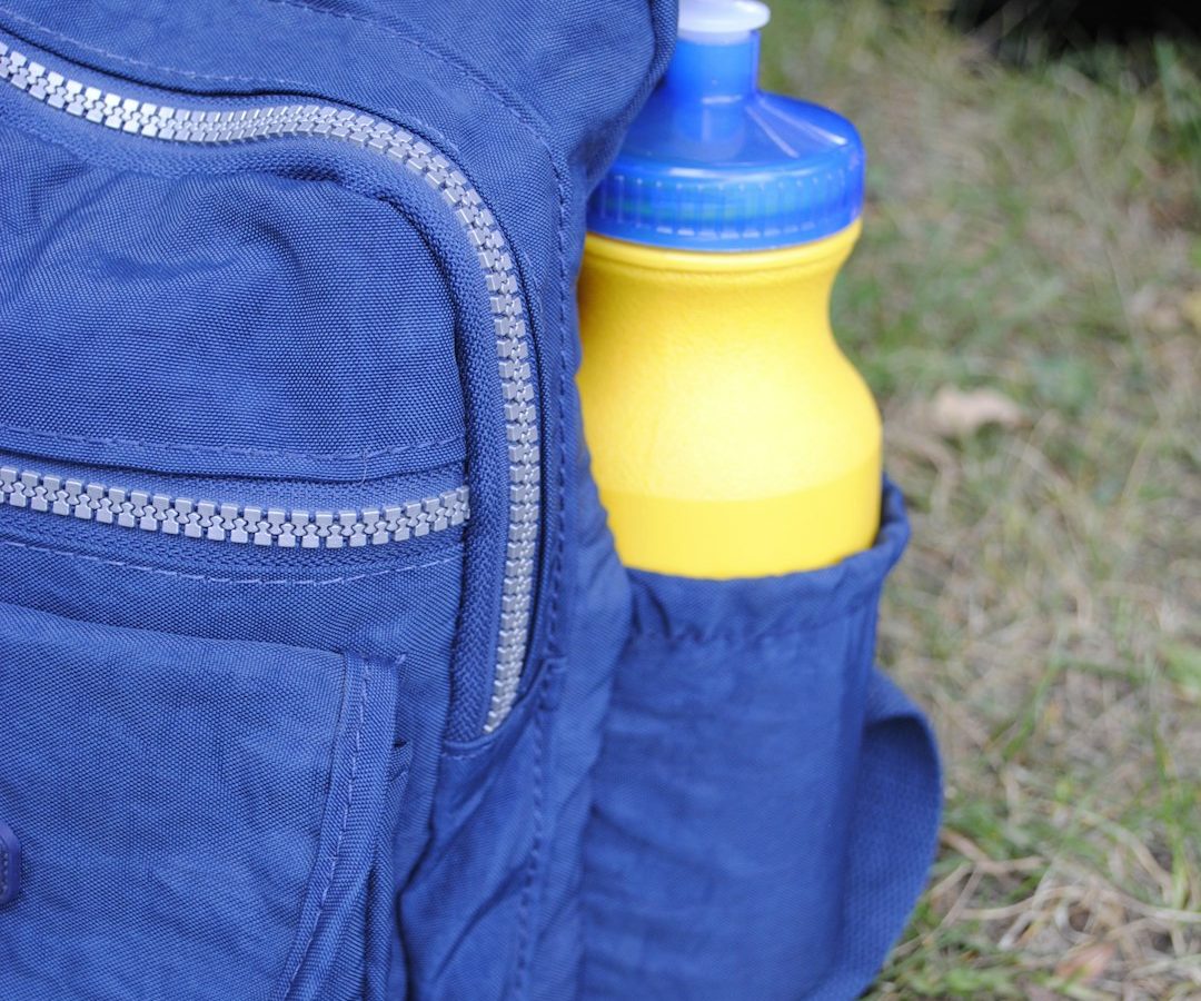 Gourde jaune rangée dans la poche latérale d’un sac à dos bleu